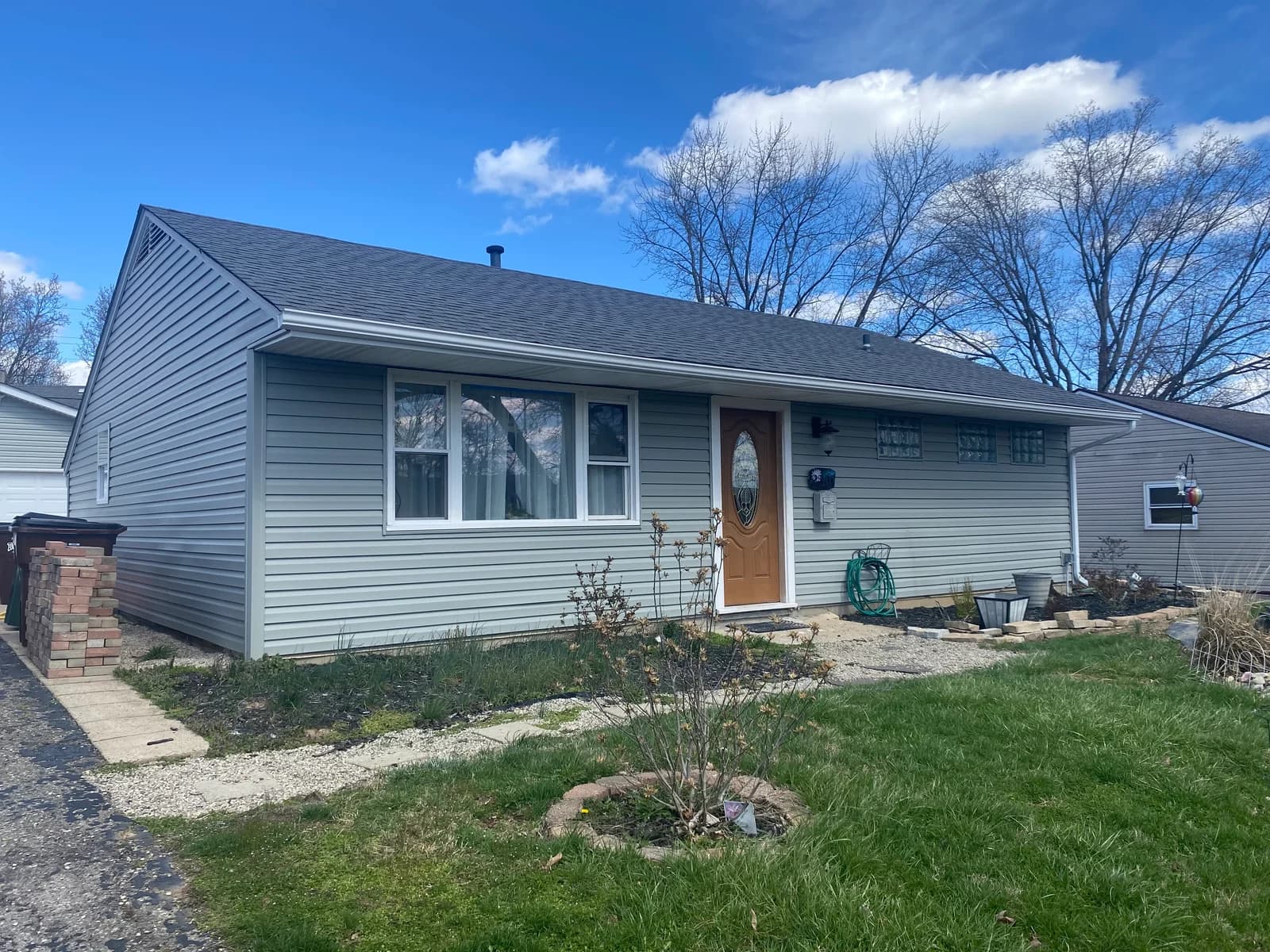House exterior with gray siding, a wooden front door, and garden beds