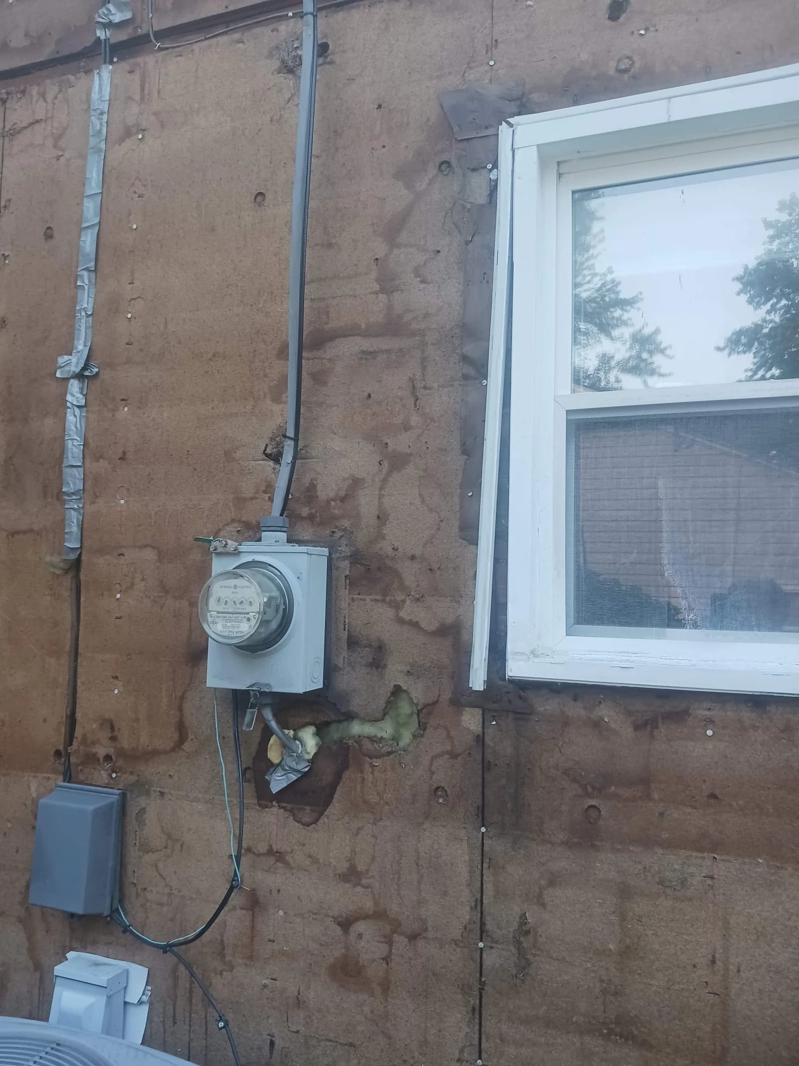 Exposed sheathing around a window and utility meter during exterior work
